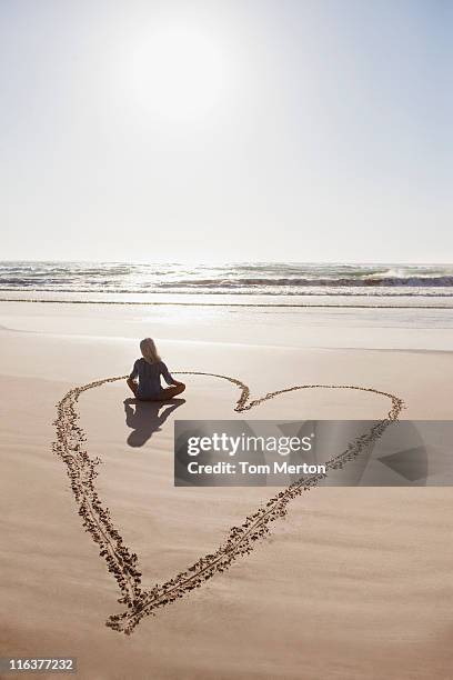 woman sitting cross-legged in heart on beach - woman in love stockfoto's en -beelden
