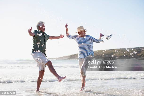 senior couple splashing in ocean - strand paar stockfoto's en -beelden