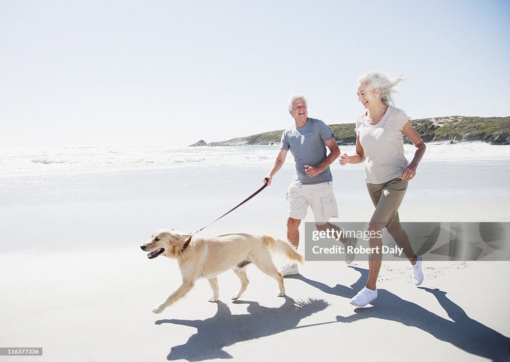 Senior Pareja corriendo en la playa con perro