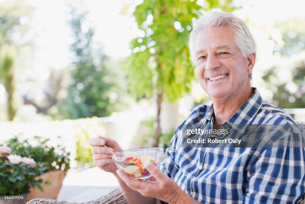 Senior man eating vegetables on patio