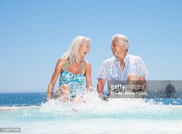 senior couple splashing in swimming pool - senior kicking stock pictures, royalty-free photos & images