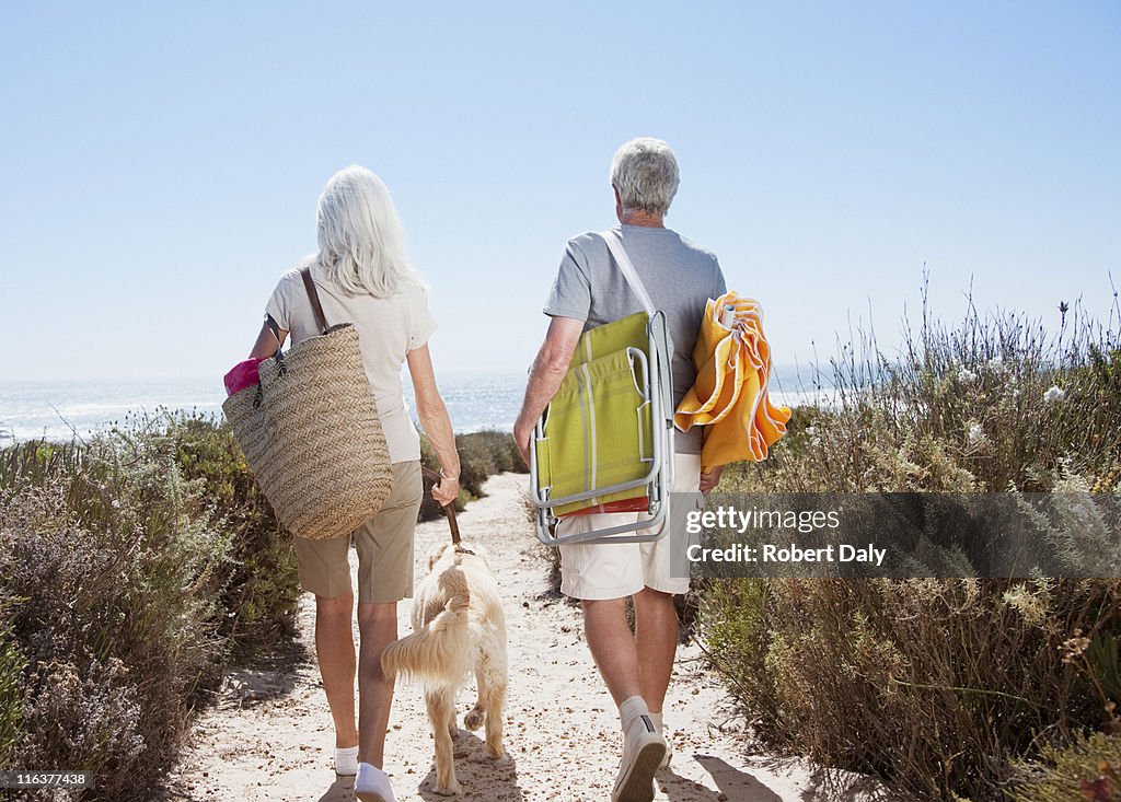 Senior couple walking on beach path with dog