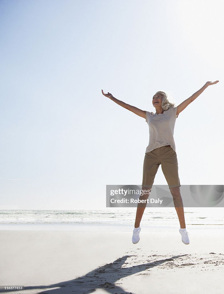 Senior woman jumping on beach