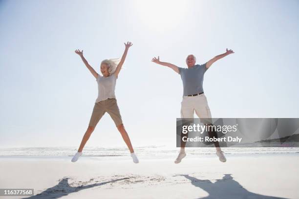 altes paar springen am strand - mann freudensprung sonne vorderansicht leger stock-fotos und bilder