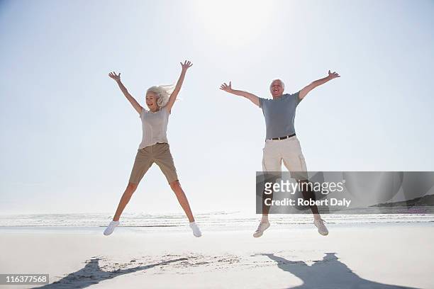 senior couple jumping on beach - man with arms raised stock pictures, royalty-free photos & images