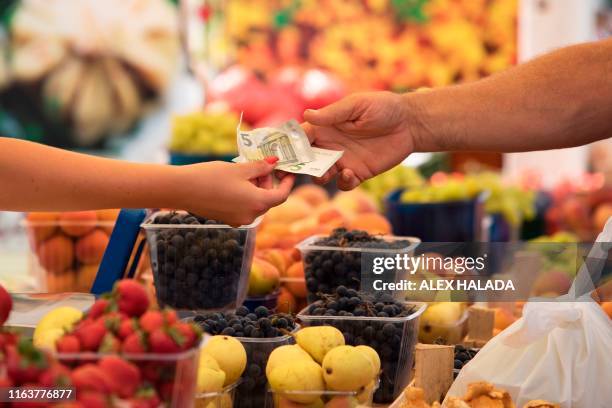 Customer pays for the shopping at a fruit stand on the Naschmarkt market in Vienna, Austria, on August 24, 2019. - A debate on whether to enshrine in...