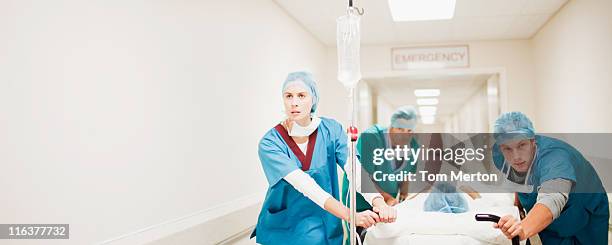 doctors pushing patient on gurney down hospital corridor - emergencies and disasters stockfoto's en -beelden