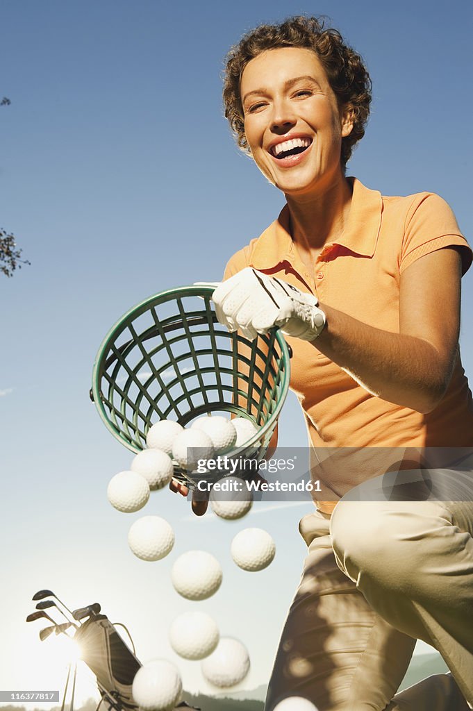 Italy, Kastelruth, Mid adult woman pouring basket of golf balls on golf course