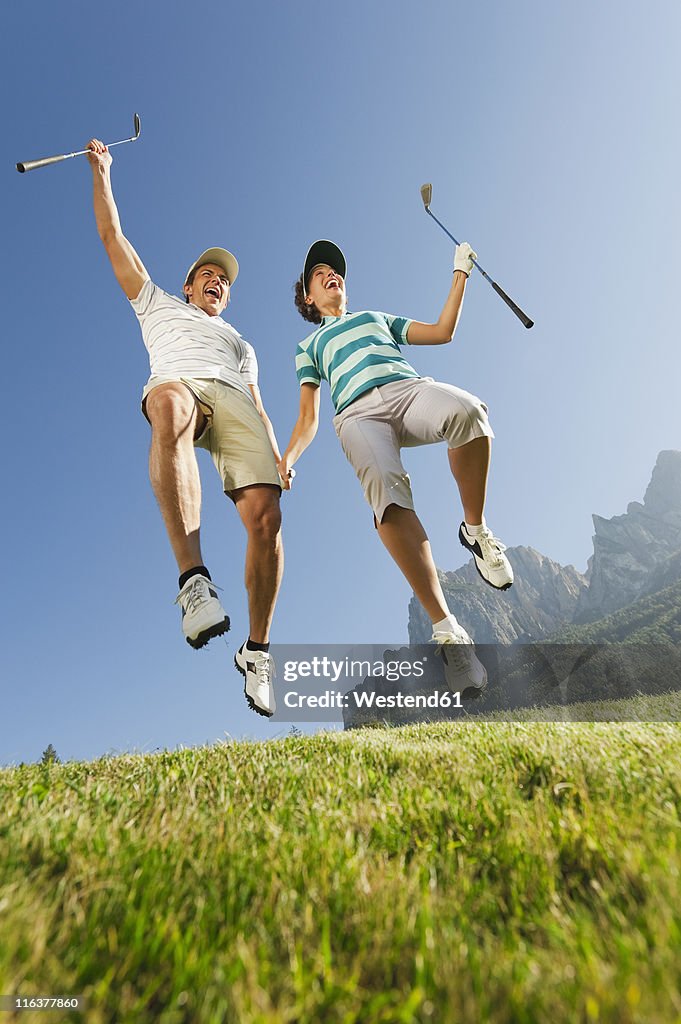 Italy, Kastelruth, Mid adult couple jumping together on golf course