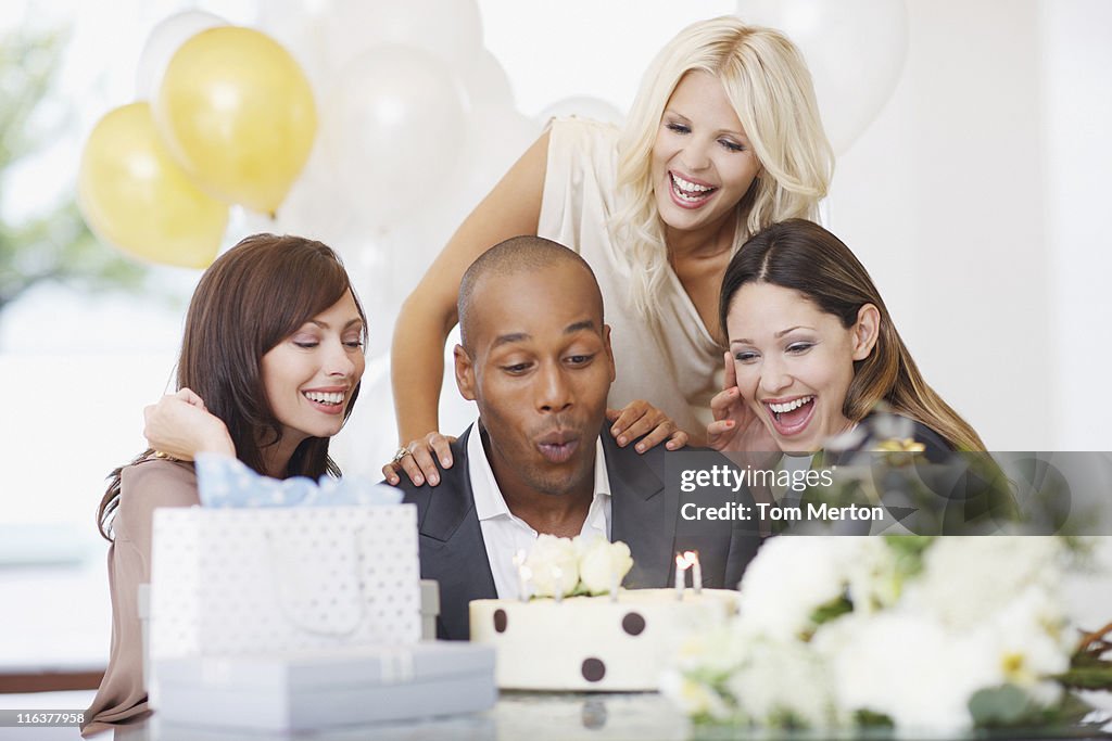 Friends watching man blow out candles on birthday cake