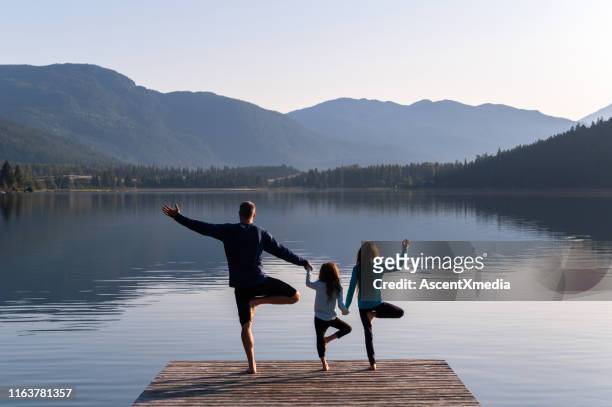 family practising yoga outdoors - tree position stock pictures, royalty-free photos & images