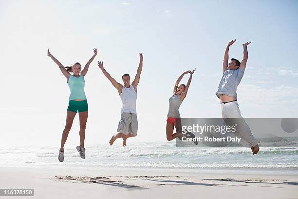 paar springen am strand - mann freudensprung sonne vorderansicht leger stock-fotos und bilder