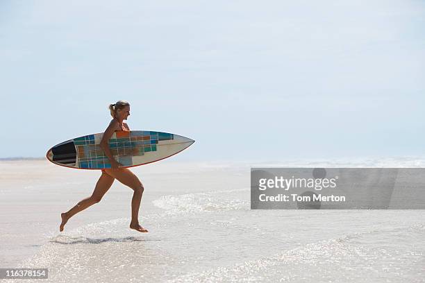 woman running on beach with surfboard - woman surfboard stockfoto's en -beelden