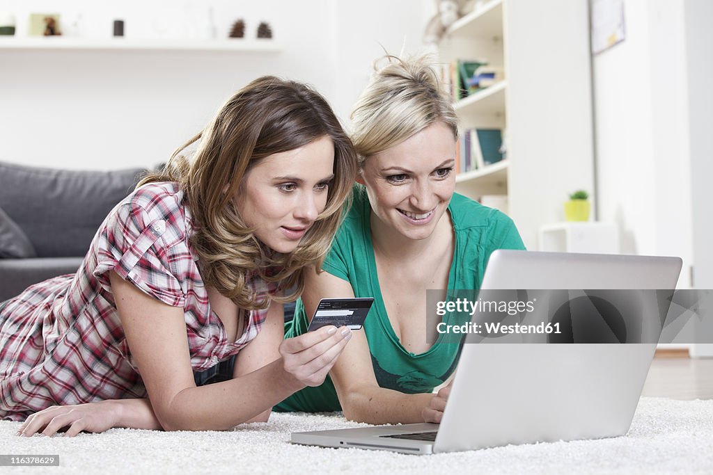 Germany, Bavaria, Munich, Young friends lying on rug and doing home shopping