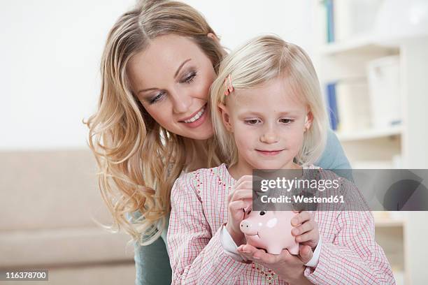 germany, bavaria, munich, mother and daughter holding piggy bank, smiling - blonde girl piggy bank stock-fotos und bilder