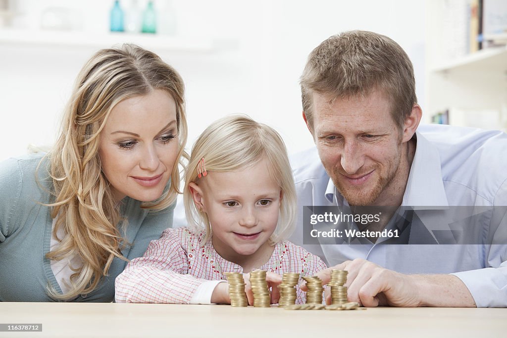 Germany, Bavaria, Munich, Parents and daughter counting coins at table, smiling