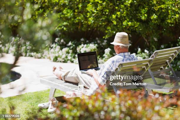 senior man on lounge chair using laptop - silver surfer stock pictures, royalty-free photos & images