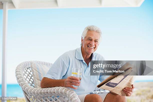 senior man reading newspaper on beach patio - holding cold drink stock pictures, royalty-free photos & images