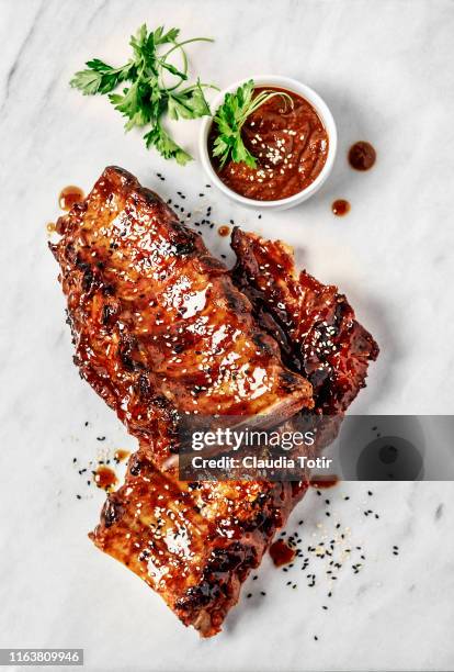 full rack of grilled barbecue ribs with barbecue sauce on a white cutting board - rippchen stock-fotos und bilder
