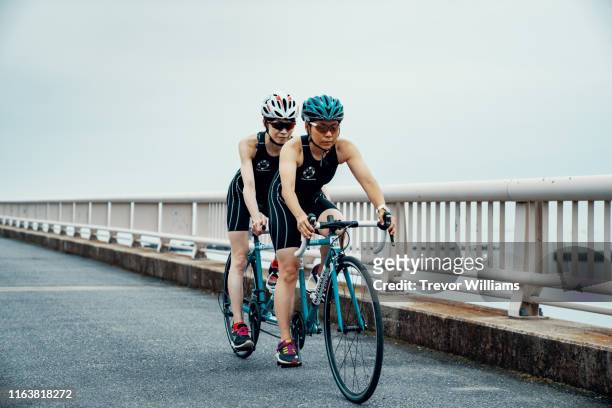 visually impaired female triathlete training together with her guide and coach on a tandem bicycle - tandem bicycle stock pictures, royalty-free photos & images