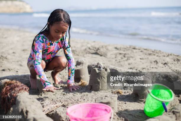 mädchen lateinamerikanischer abstammung sitzen auf dem sand bauen den sandburgen mit eimern und schaufeln. - kind sandburg stock-fotos und bilder