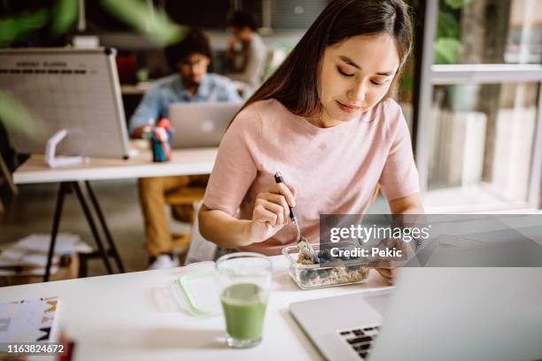 young asian blogger having vegetarian breakfast at work - breakfast work stock pictures, royalty-free photos & images