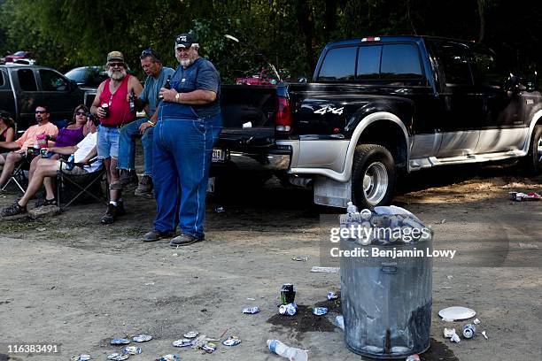 An overflowing garbage can of beer bottles and cans sits on the beach as revelers drink beer and lounge on the riverfront during the Redneck Fishing...