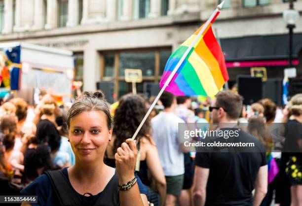 frau winkt regenbogen-flagge bei gay pride parade auf der stadtstraße - pride london stock-fotos und bilder