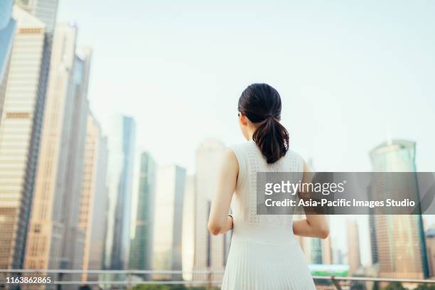 rückansicht der asiatischen jungen geschäftsfrau mit blick auf die finanzhochhäuser im lujiazui financial district, shanghai,china - japanese bussiness woman looking up stock-fotos und bilder