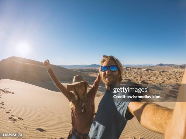 paar reisen nimmt selfie-foto auf sanddünen bei sonnenuntergang - couple dunes stock-fotos und bilder