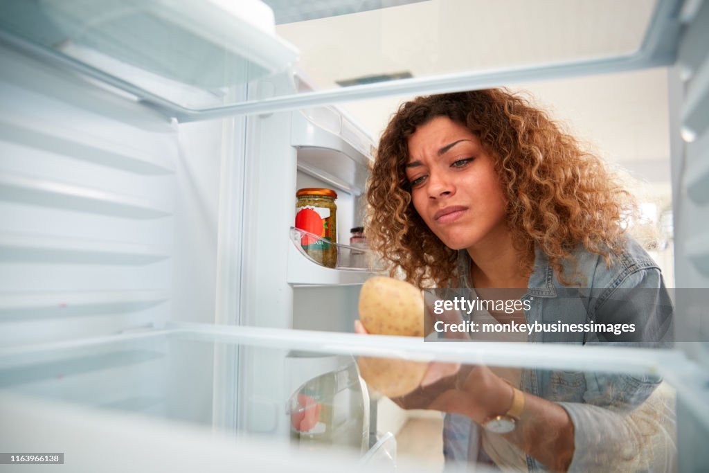 Mulher disappointed que olha dentro do refrigerador vazio à exceção da batata na prateleira