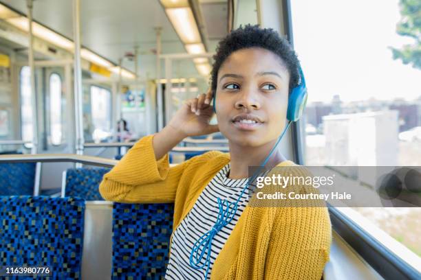 beautiful african american young woman listens to music with headphones while riding commuter train in the city - commuter train stock pictures, royalty-free photos & images
