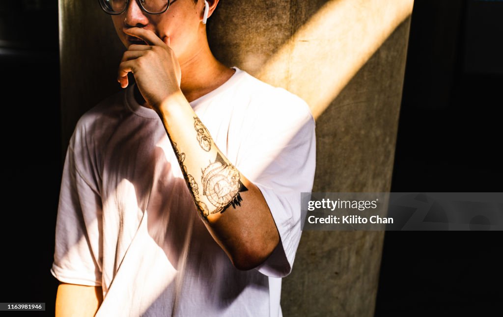 Young asian man with sleeve tattoo covering his mouth with one hand