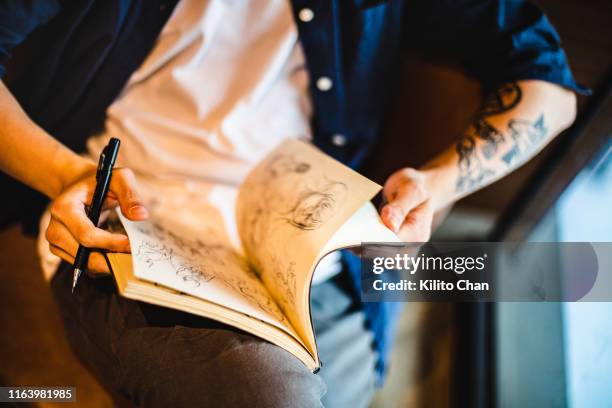asian young man sitting and doing a sketch on a notebook - schetsblok stockfoto's en -beelden