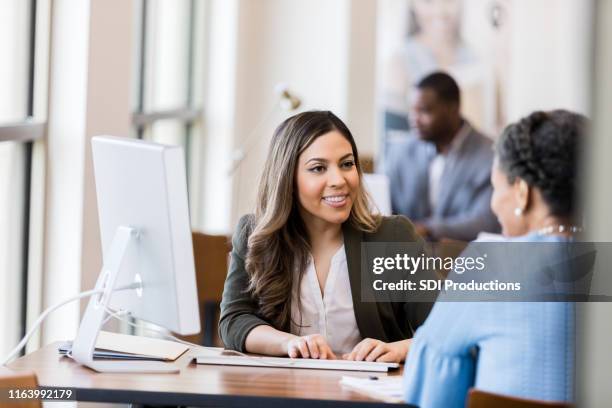bank manager smiles at customer as she types in information - bank manager stock pictures, royalty-free photos & images