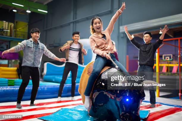 happy young chinese friends playing mechanical bull game - bucking bronco stock-fotos und bilder