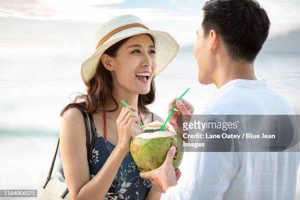 happy young chinese couple drinking coconut milk on beach - coconut water stock pictures, royalty-free photos & images