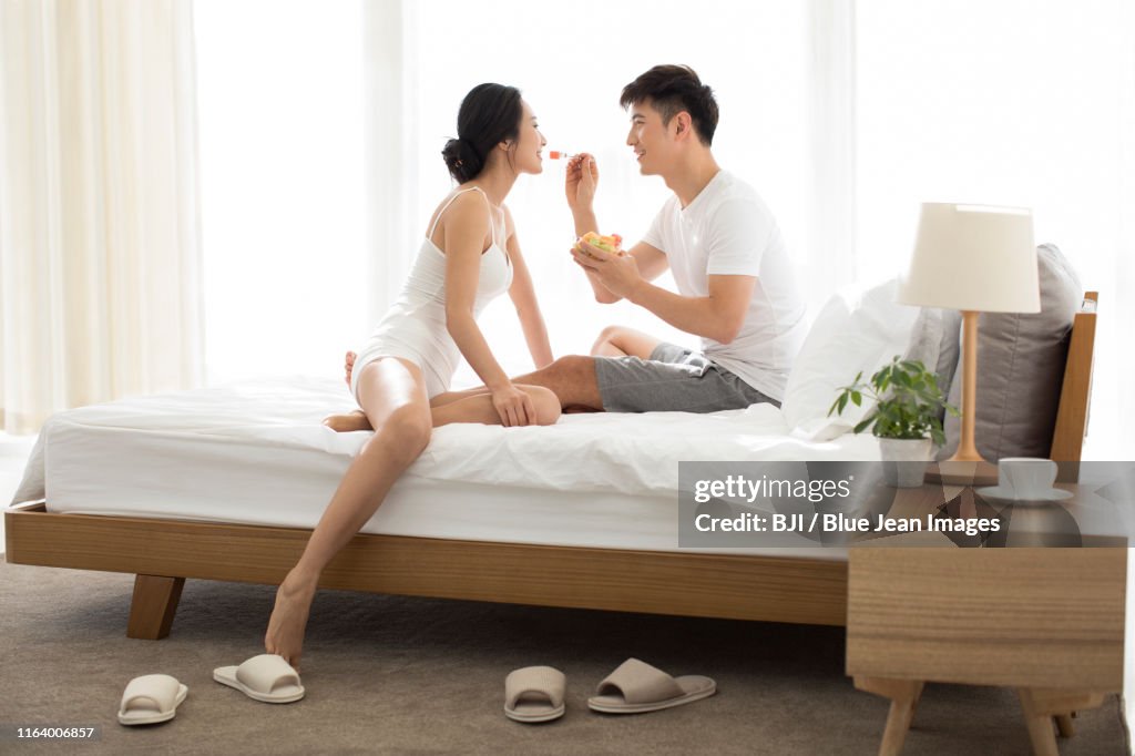 Happy young couple eating fruit salad on bed