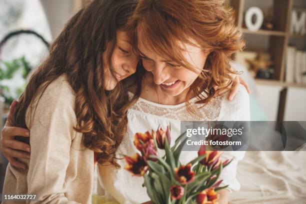 gelukkige moeder en dochter knuffelen en houden een boeket van verse bloemen - mother day stockfoto's en -beelden