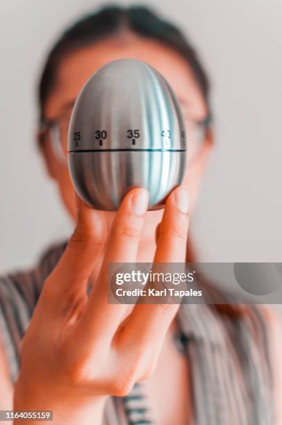 a woman is holding a metal kitchen timer on a white background - lancetta dei minuti foto e immagini stock