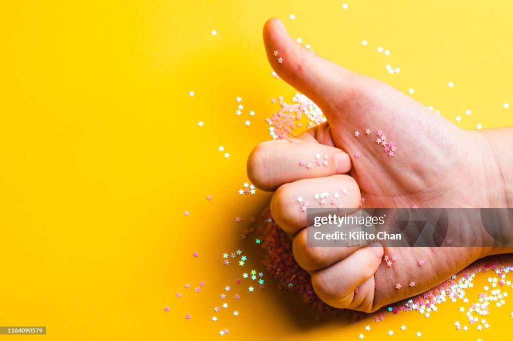 Thumb up with glittering litter stars against yellow background