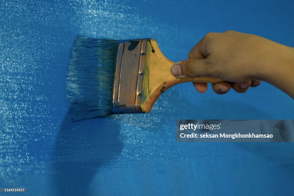 Close-up of a person's hand painting a wall with a paintbrush