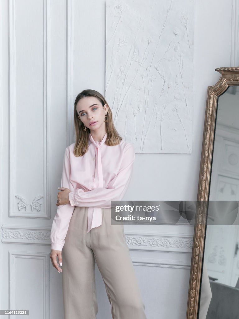 美麗的年輕女子穿著復古粉紅色上衣和米色褲子在巴黎公寓