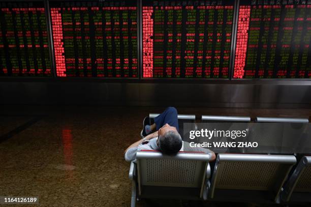 An investor rests on a chair in front of screens showing stock market movements at a securities company in Beijing on August 26, 2019. - Asian equity...