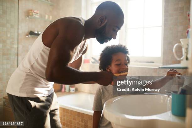 A boy in the bathroom brushing his teeth with his dad in the morning with bamboo toothbrush