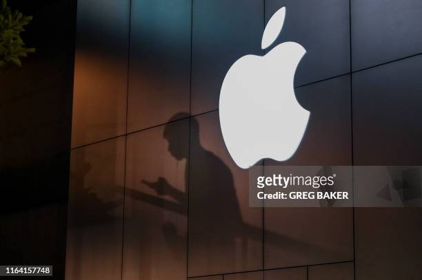 The shadow of a man is cast on the wall of an Apple store as he uses his mobile phone in Beijing on August 26, 2019. There were signs of a thaw in...