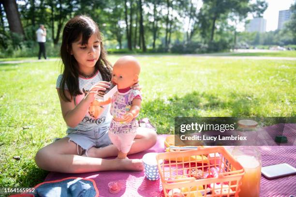 seven year old girl playing mother to her doll at a picnic in the park - doll fotografías e imágenes de stock