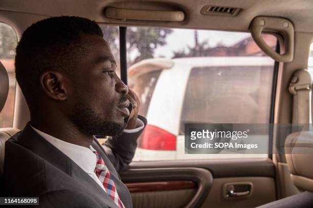 Bobi Wine talks on the phone while driving through Kampala, at the beginning of a day of campaigning. Bobi Wine, whose real name is Robert...