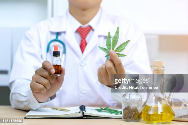 man scientist in laboratory testing oil extracted from a marijuana plant. saving notes and results on a paper. - cannabis oil - fotografias e filmes do acervo