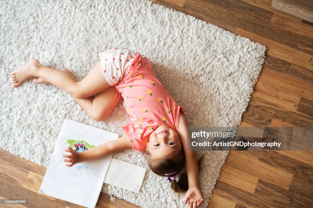 Piccola ragazza carina sdraiata sul tappeto a casa e sorridente.